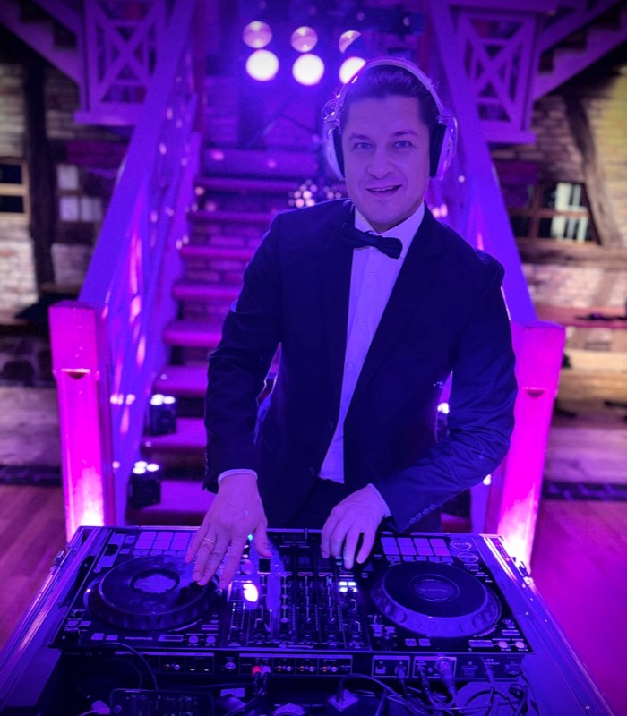 DJ Edouard im Smoking mit Kopfhörern am DJ-Pult, lachend, im violetten Bühnenlicht