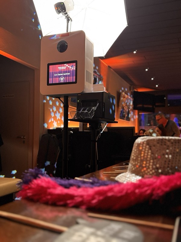 Fotobox mit Softbox im Einsatz auf einer Feier, davor Glitzerhut und Federboas